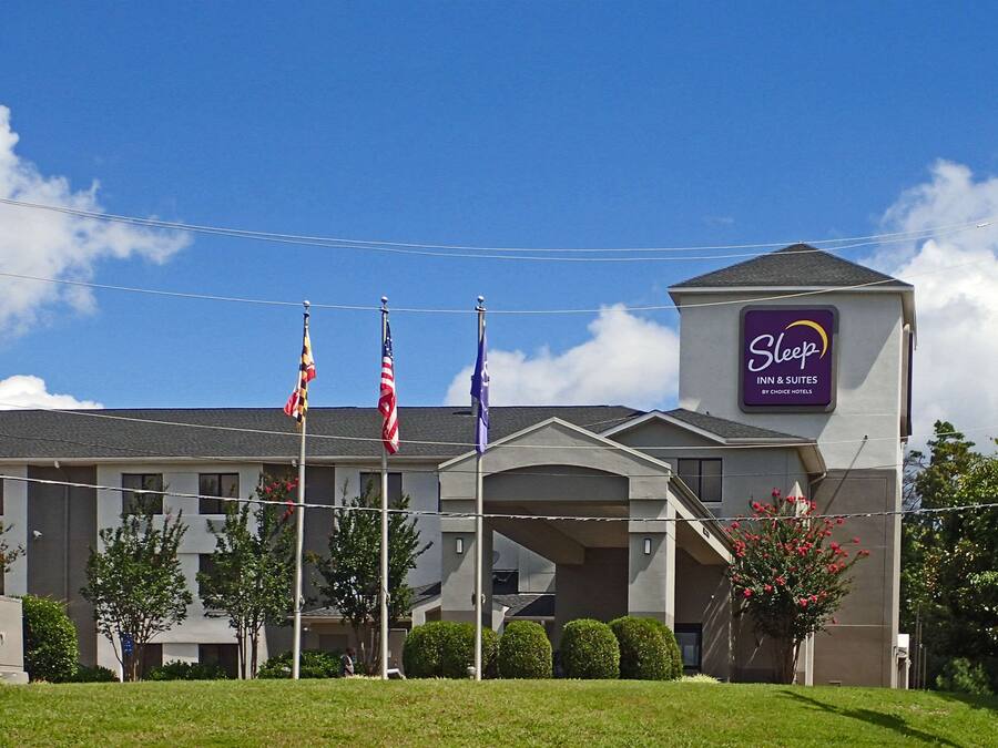 Ein Sleep Inn & Suites Hotel der Choice Hotels mit mehreren Flaggen, blauem Himmel und gepflegter Bepflanzung.