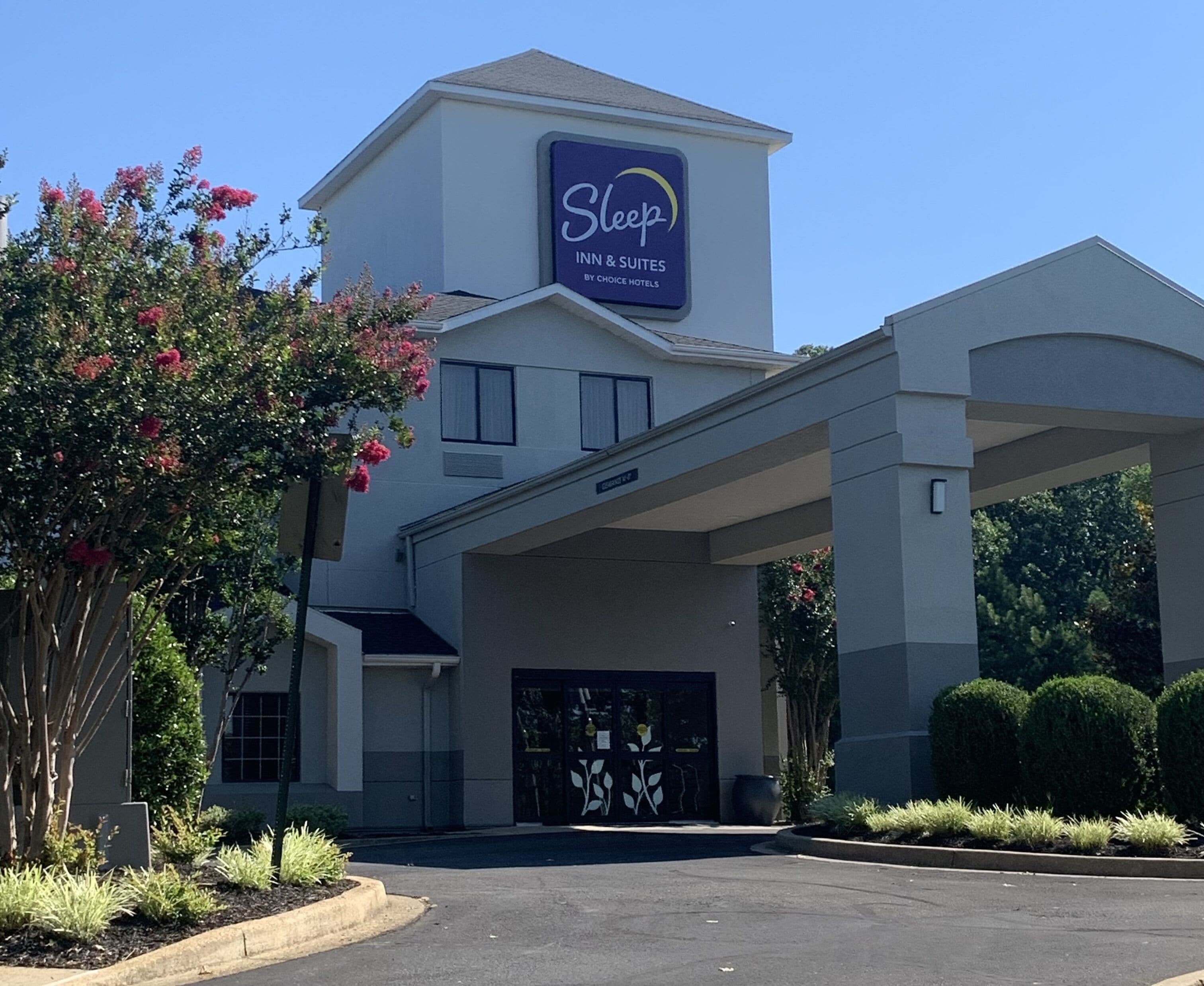 Edificio de Sleep Inn & Suites by Choice Hotels con entrada despejada, zona de estacionamiento techada y jardines bien cuidados.
