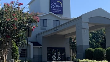 Edificio de Sleep Inn & Suites by Choice Hotels con entrada despejada, zona de estacionamiento techada y jardines bien cuidados.