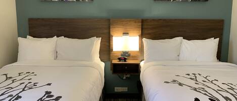Une chambre d’hôtel avec deux lits, une tête de lit en bois, une table de chevet avec une lampe et des œuvres d’art murales.