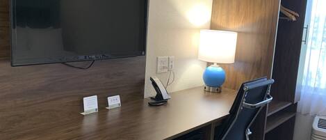 Een hotelkamer met een flatscreen televisie aan de muur, een bureau met een lamp, een magnetron, een minibar en een stoel.