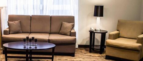 A living room with a sofa, armchair, coffee table, lamp, and patterned carpet.