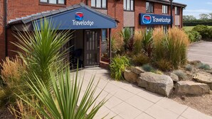 A Travelodge hotel with a brick facade, a covered entrance, and landscaped surroundings. - Travelodge Cambridge Swavesey (Cambridge)