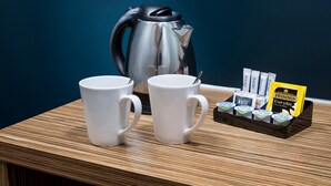 A wooden table with two white mugs, a stainless steel coffee pot, and a tray of Twinings tea packets. - Travelodge Cambridge Swavesey (Cambridge)