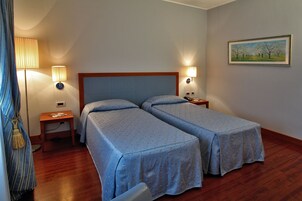 Una habitación de hotel con dos camas, una mesita de noche, una lámpara y un cuadro en la pared.