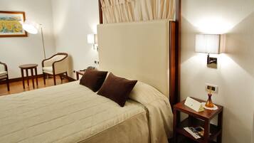 Habitación de hotel con una cama grande, dos sillas, una mesita con lámpara y un aplique de pared.