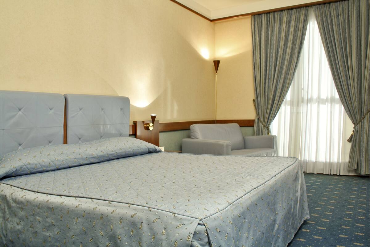 Une chambre d’hôtel avec un grand lit, un petit canapé, une table de chevet et une fenêtre avec des rideaux.