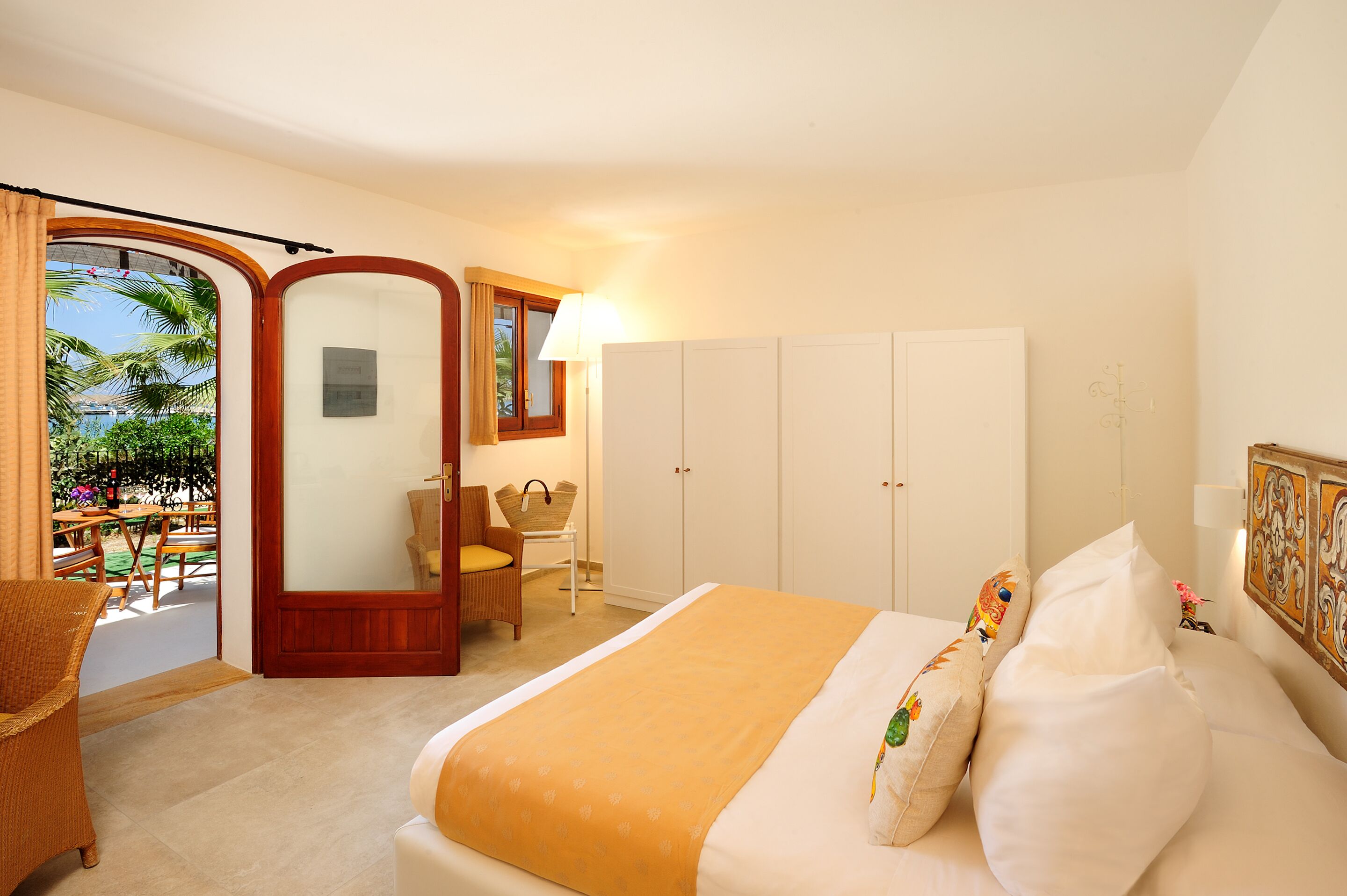 A hotel room with a bed, a wardrobe, a chair, a table, and a view of the outdoors.