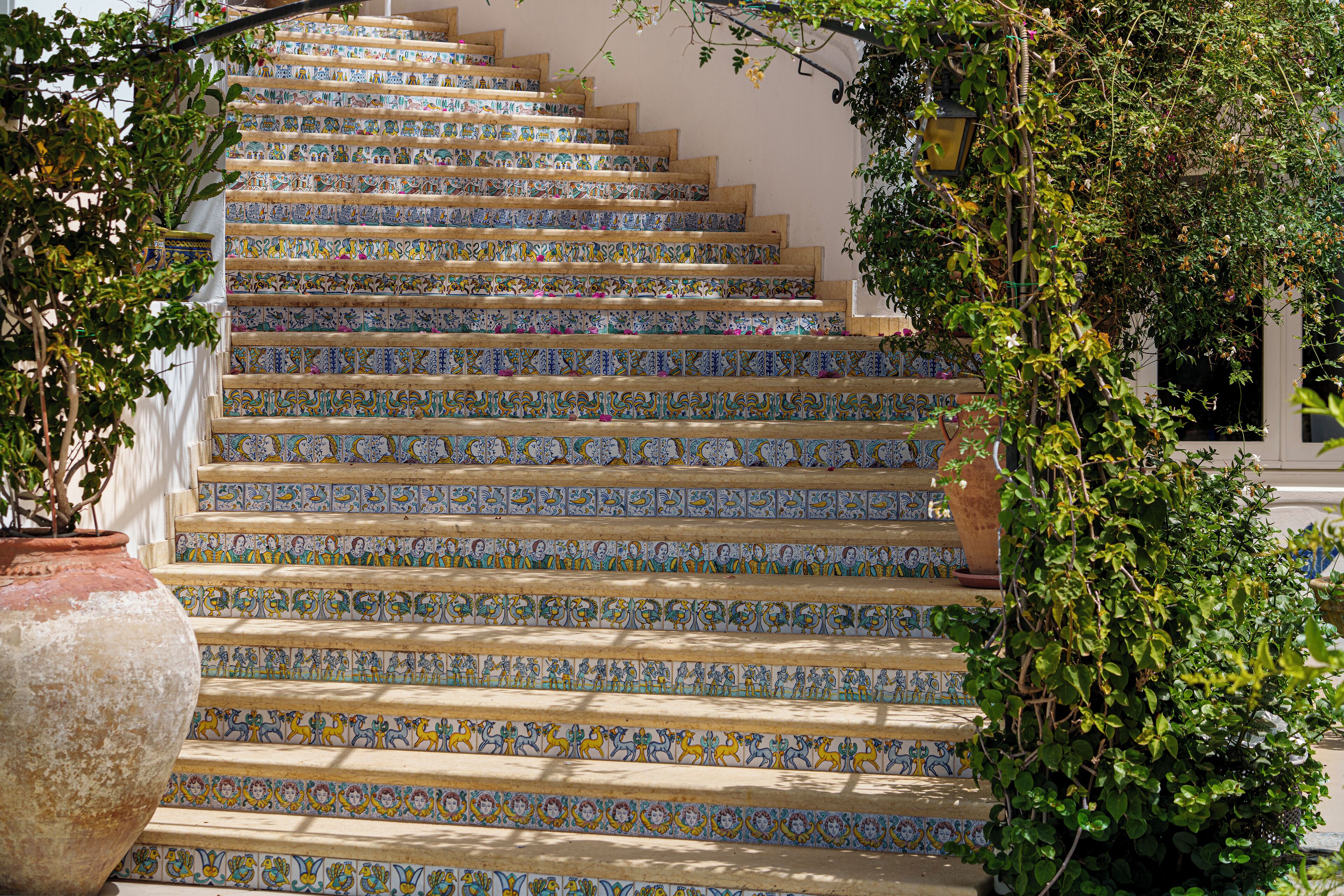 Un escalier orné de carreaux colorés et, à gauche, un grand pot de fleurs.