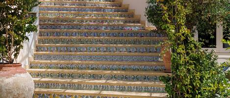 Un escalier orné de carreaux colorés et, à gauche, un grand pot de fleurs.