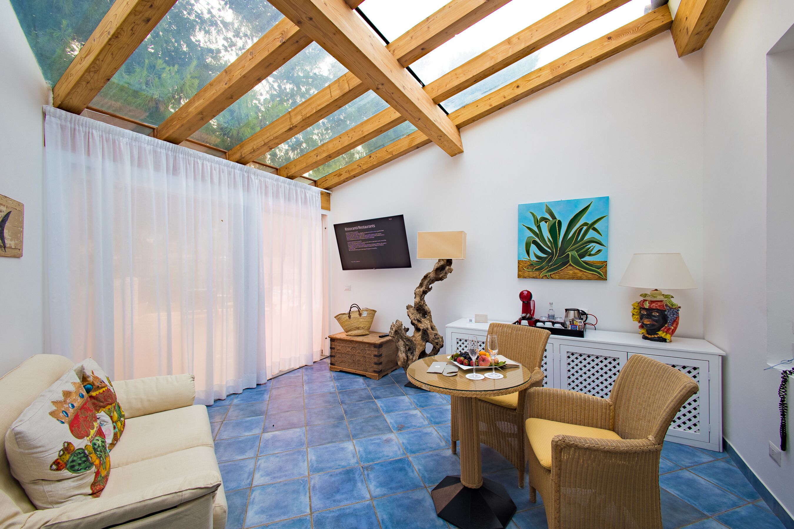 Un'accogliente stanza con soffitto in legno, un divano con un cuscino colorato, un tavolo da pranzo con sedie e una TV a parete.
