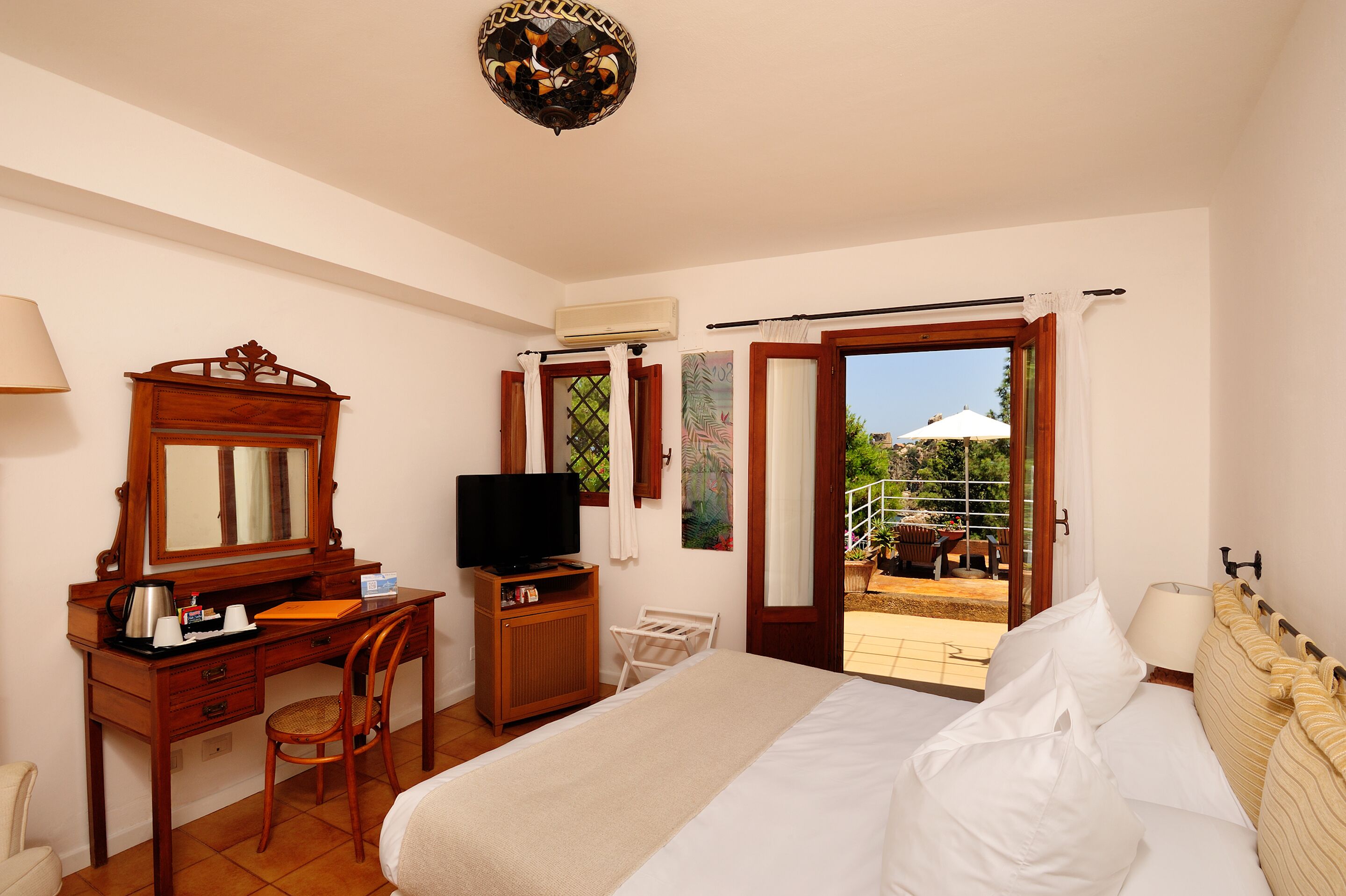 Ein Hotelzimmer mit Bett, Schreibtisch mit Fernseher, Stuhl und Blick auf den Außenbereich.