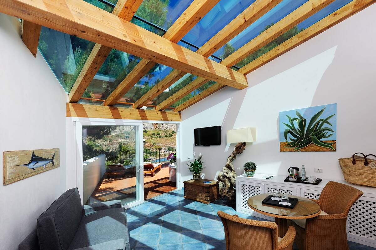 A sunlit room with a glass ceiling, a TV, a painting, and a dining area with a table and chairs.