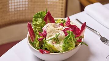 A bowl of salad with mixed greens and a creamy dressing, placed on a table with a white tablecloth.