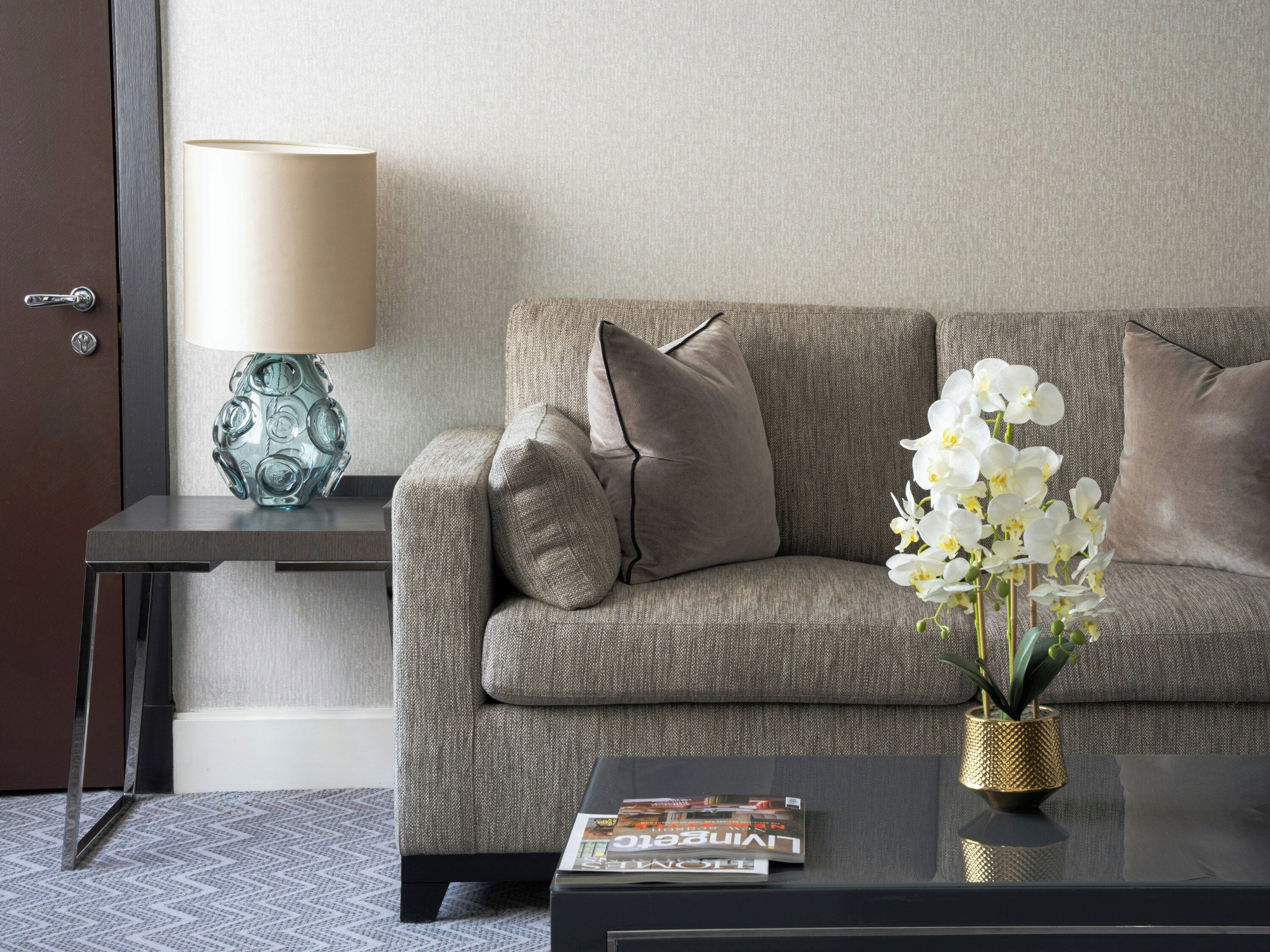 A modern living room with a grey sofa, a side table with a lamp, and a magazine on a coffee table.