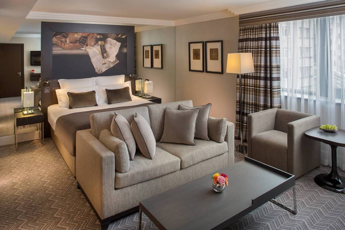 Ein Hotelzimmer mit einem Bett, einem Schlafsofa, einem Sessel, einem Couchtisch, einem Fernseher und einem Bild an der Wand.