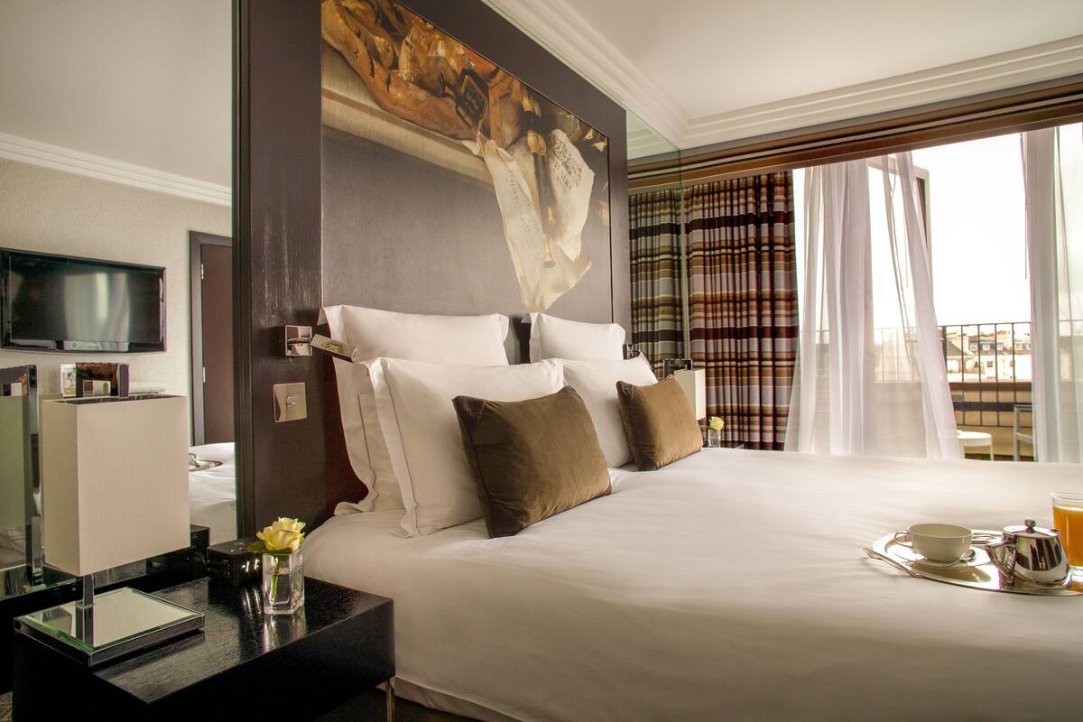 Ein Hotelzimmer mit einem großen Bett, einem Flachbildfernseher, einem Nachttisch mit Blumenvase und einem Frühstücksbrett auf dem Bett.