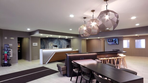 Een moderne hotel lobby met een receptiebalie, een zithoek en een groot digitaal scherm.