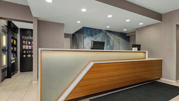 A reception area with a wooden reception desk, a wall-mounted screen, and a vending machine to the left.