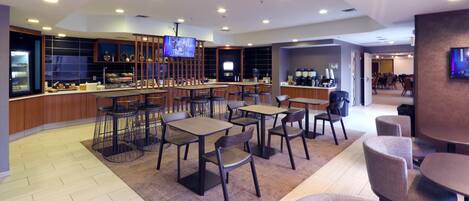 A modern cafe with multiple seating areas, a bar, and a television screen.