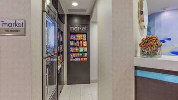 A hallway with a refrigerated display and a vending machine, leading to a market area with various packaged goods.