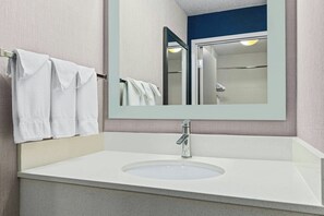 Un baño con lavamanos blanco, un espejo y un perchero para toallas.