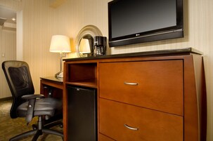 Una habitación de hotel con un escritorio de madera, una silla de oficina negra, un televisor de pantalla plana, una cafetera y un refrigerador.