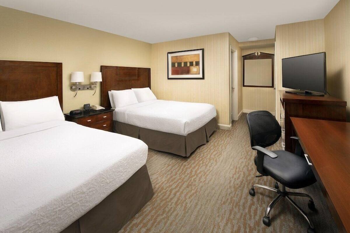 A hotel room with two beds, a desk, a chair, a television, and a framed picture on the wall.