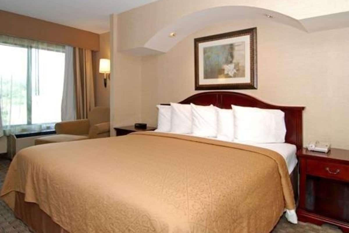 Una camera d'albergo con un letto grande, un comodino, una sedia e una finestra con tende.