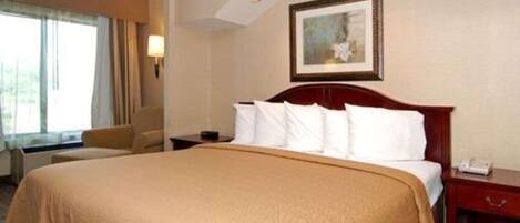 Ein Hotelzimmer mit einem großen Bett, einem Nachttisch, einem Sessel und einem Fenster mit Vorhängen.