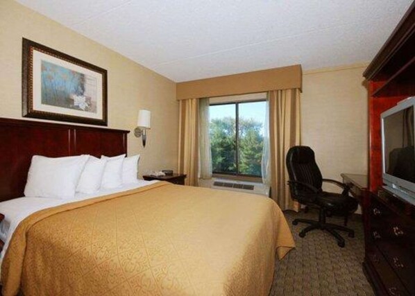 Una habitación de hotel con una cama grande, un escritorio con silla, un televisor y una ventana con cortinas.