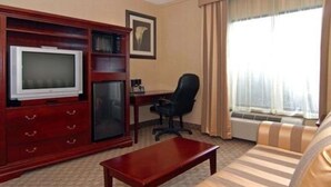 A hotel room with a television, a desk, a chair, a sofa, and a window with curtains. - Quality Inn & Suites Bensalem (Bensalem)
