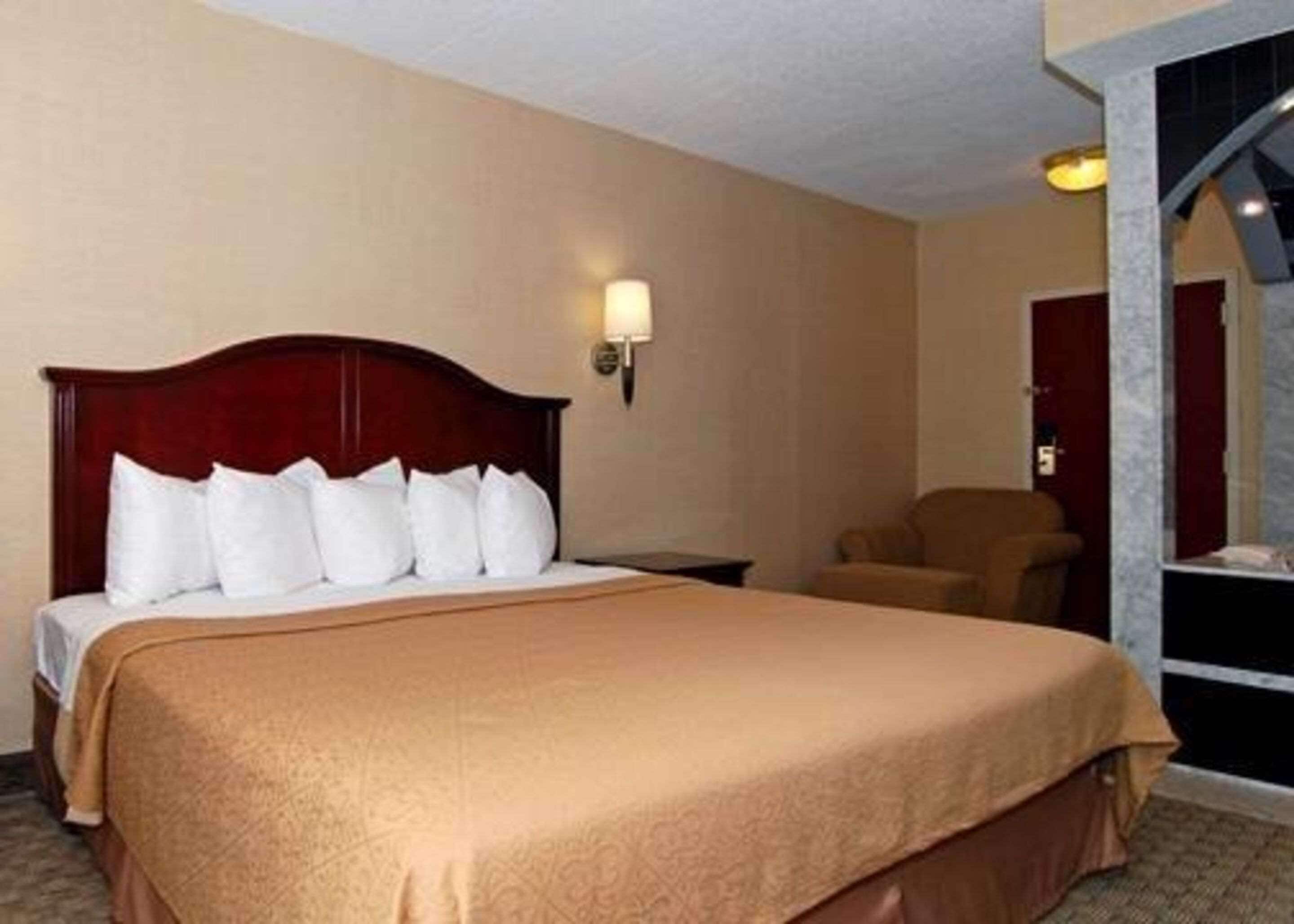 A hotel room with a large bed, a wooden headboard, and a single bedside table.