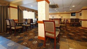 A hotel dining area with multiple tables and chairs, patterned carpet, and a large pillar. - Quality Inn & Suites Bensalem (Bensalem)