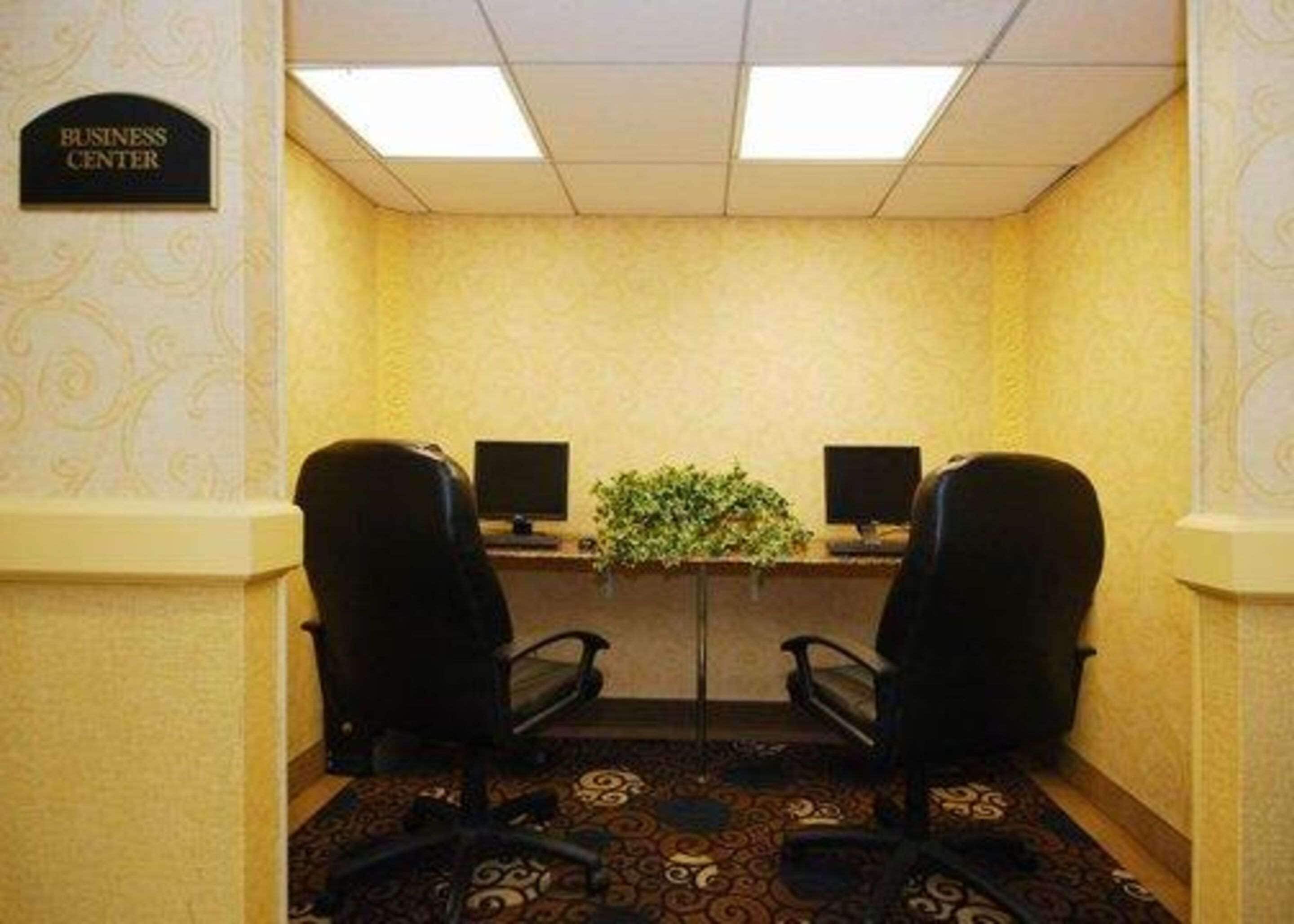 A business center with two black office chairs, a desk with two monitors, and a plant on the wall.