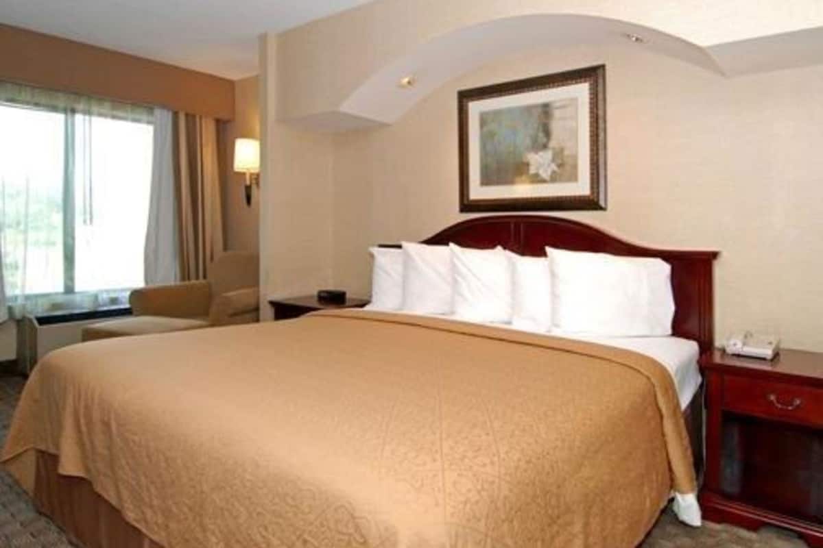 Una camera d'albergo con un letto grande, un comodino, una sedia, una lampada e un quadro appeso al muro.