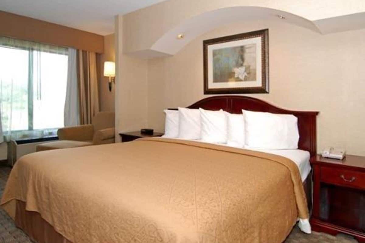 Una camera d'albergo con un letto grande, un comodino, una sedia, una lampada e un quadro appeso al muro.