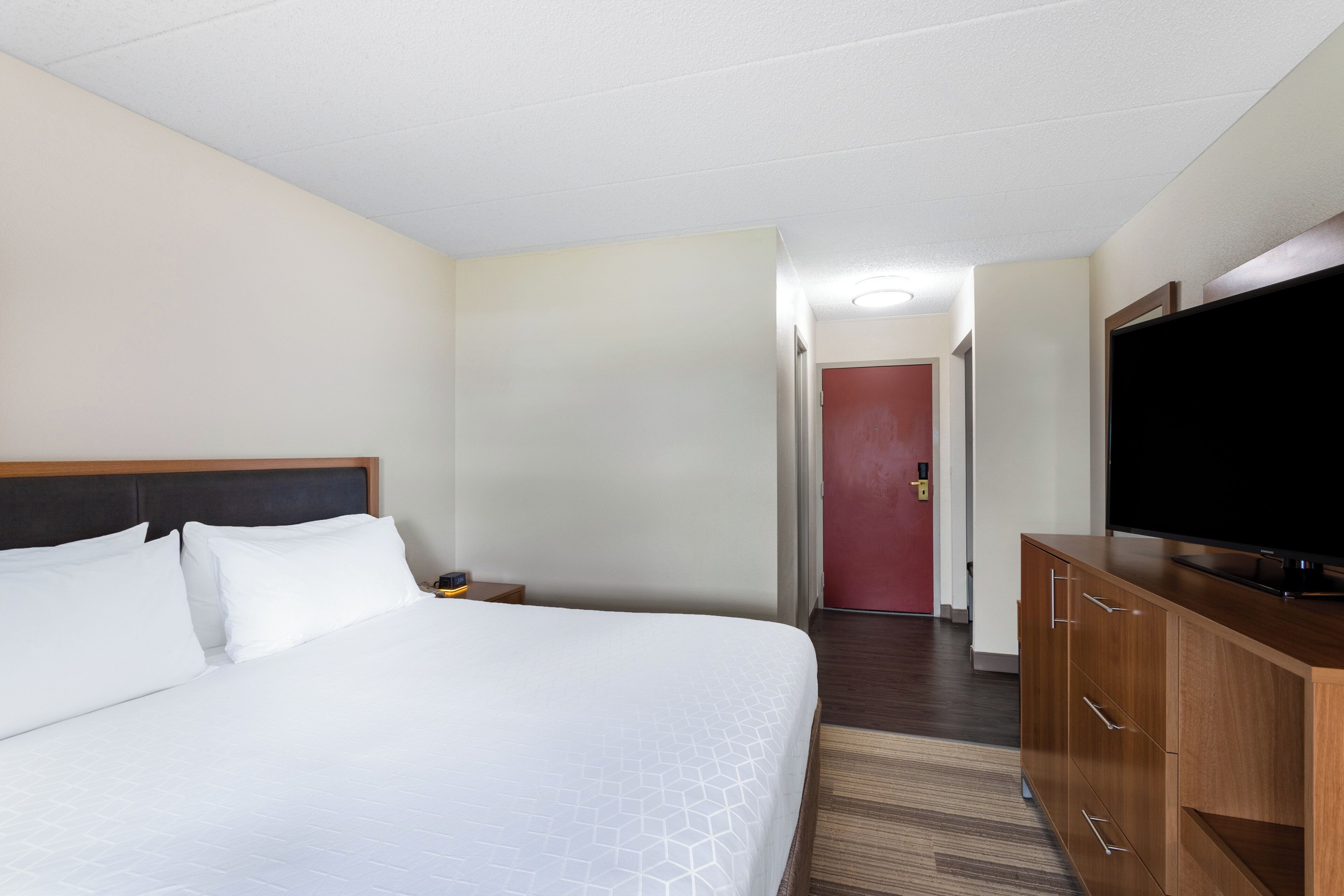 Une chambre d’hôtel avec un lit, une télévision, une commode en bois et une porte donnant sur une autre pièce.