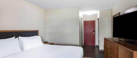 A hotel room with a bed, a TV, a wooden dresser, and a door leading to another room.