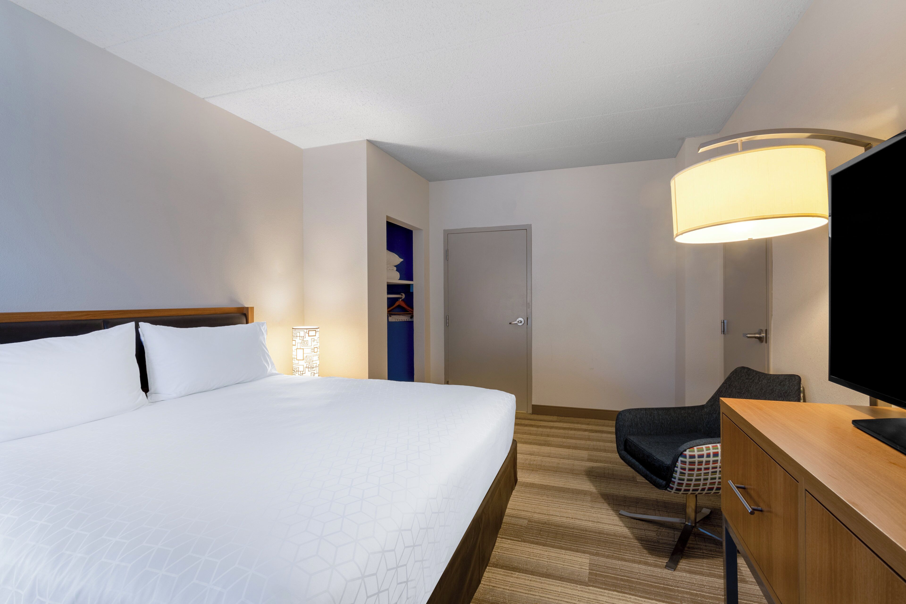 Ein Hotelzimmer mit einem großen Bett, einem Schreibtisch, einem Sessel, einem Fernseher und einer Tür.