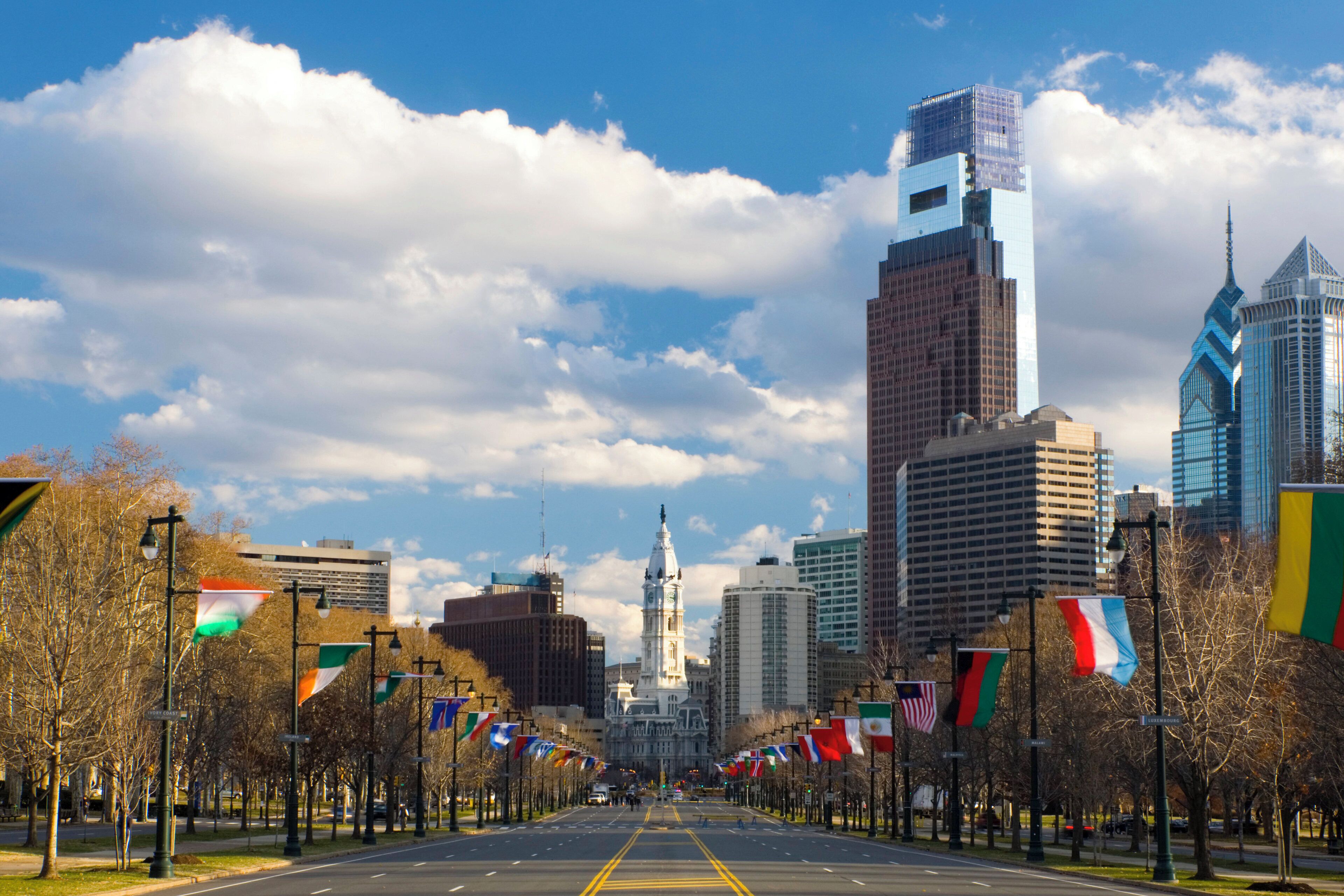 A city street lined with flags, leading to a prominent building with a clock tower.