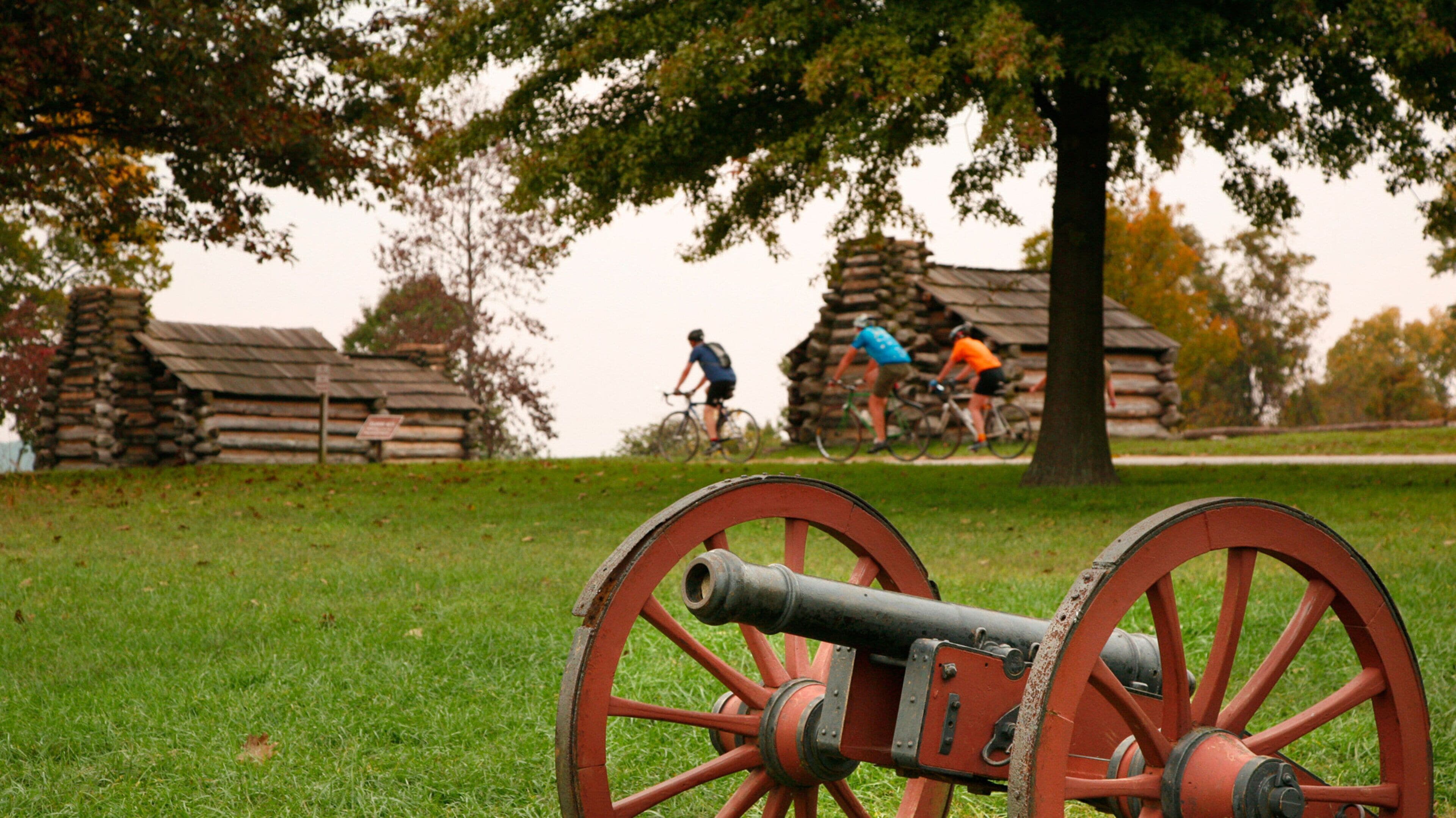 A cannon in a grassy field with cyclists in the background.