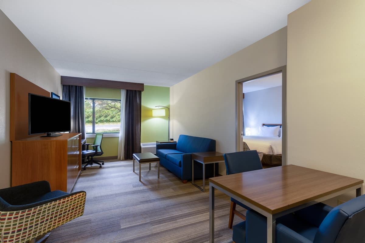 A hotel room with a flat-screen TV, a sofa, a dining table, and a chair.
