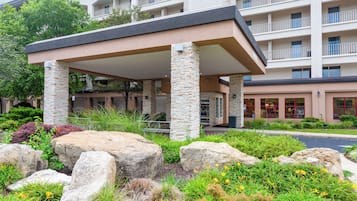 A hotel entrance with a covered patio, stone pillars, and a landscaped garden with rocks and plants.
