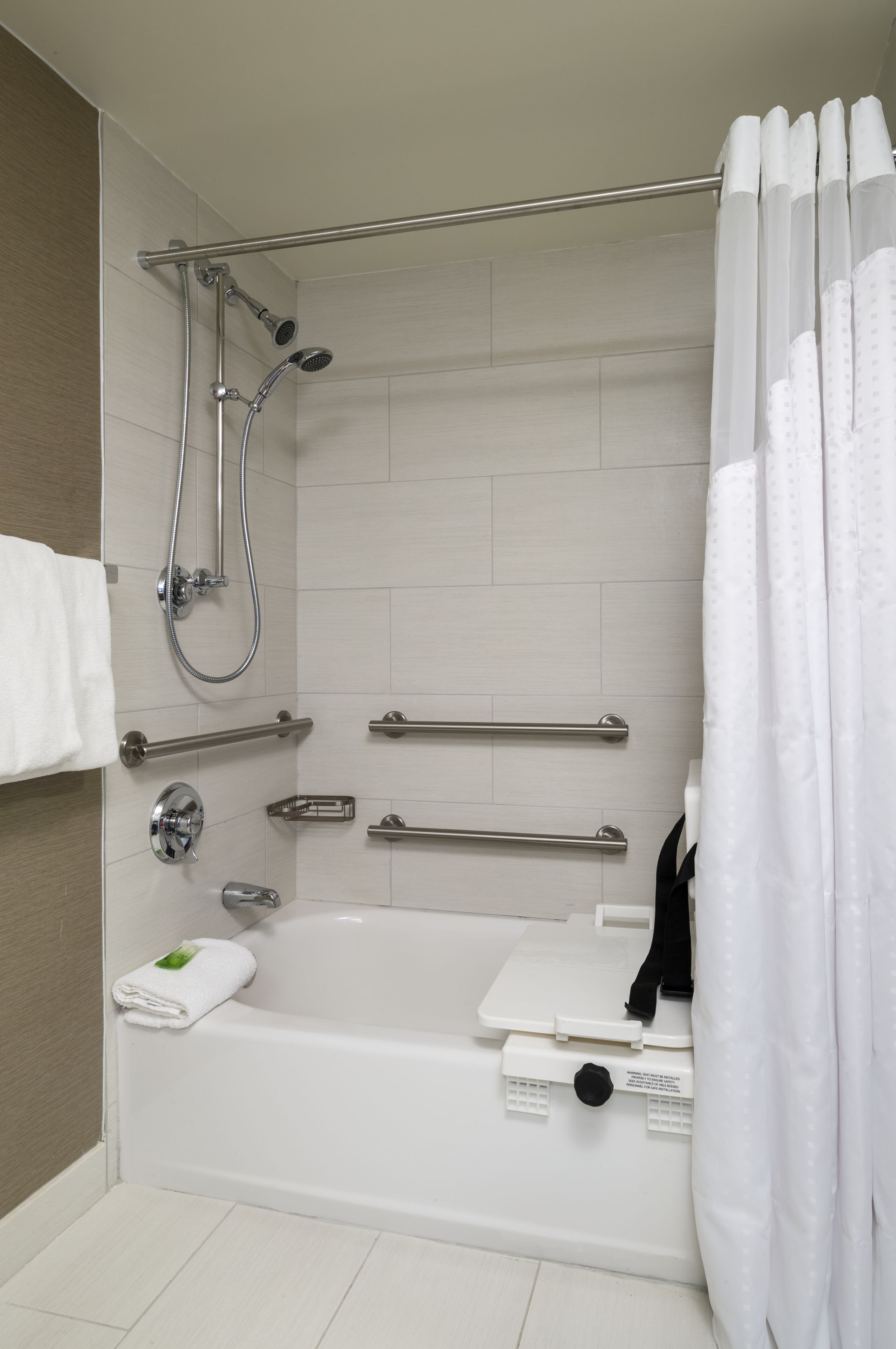 Une salle de bain moderne avec une baignoire, une douche, des barres d’appui et une serviette blanche.
