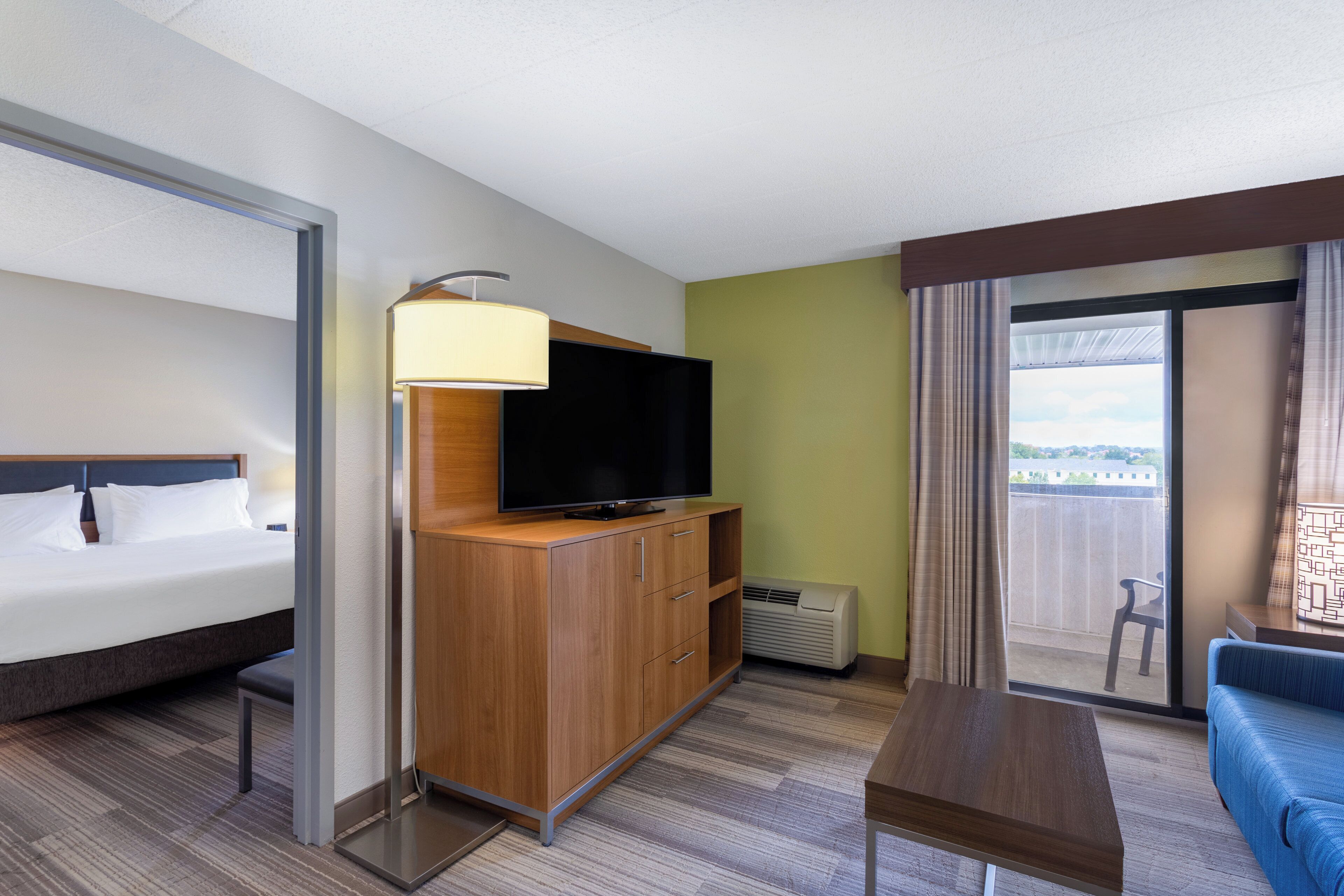 Habitación de hotel con una cama, un televisor sobre un mueble de madera, una mesita y vistas al exterior a través de una ventana.