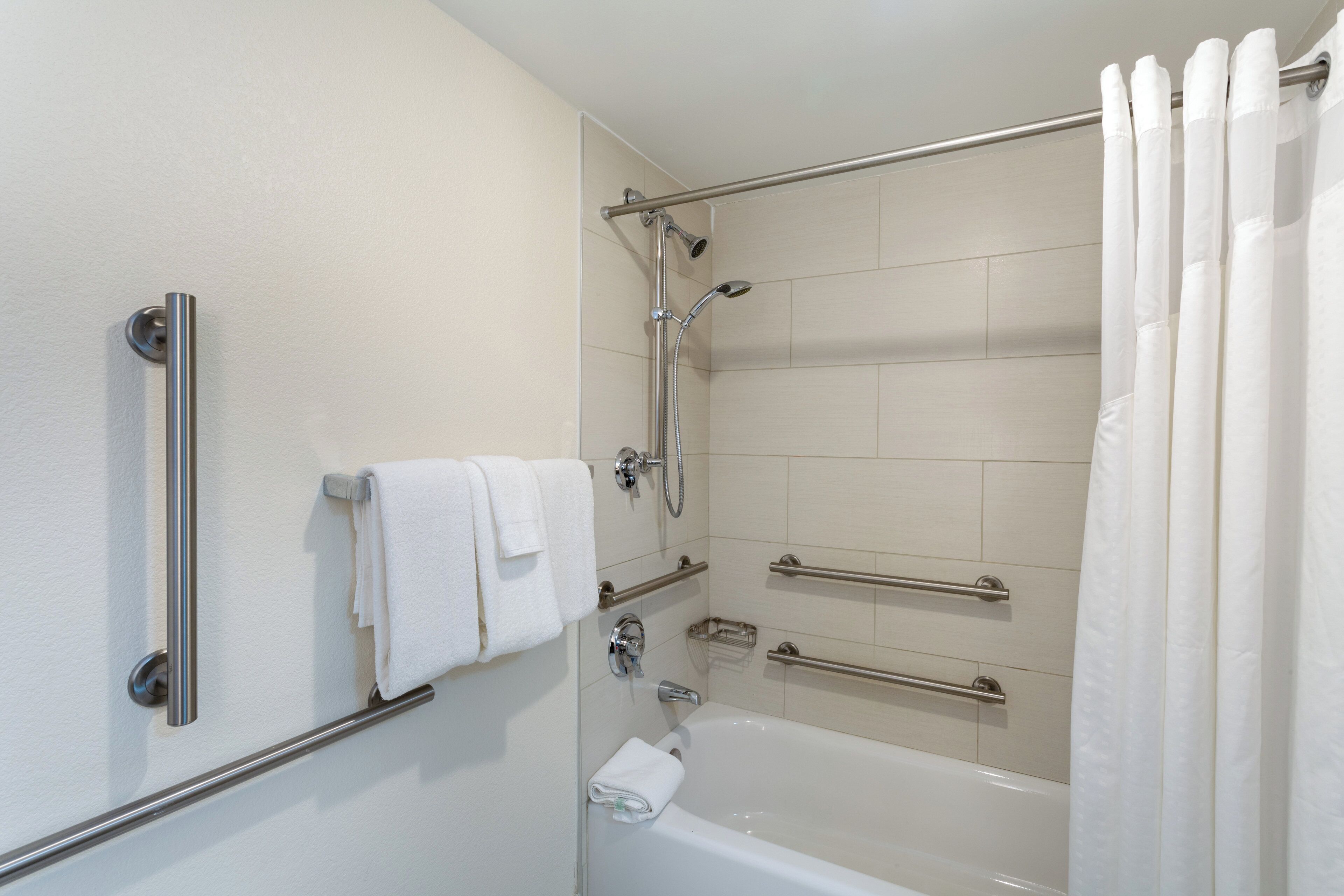 A bathroom with a bathtub, a shower, and a toilet. There are grab bars installed for safety.