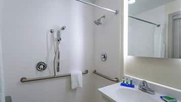 Un baño con ducha, barras de apoyo, toallero, lavabo con artículos de aseo y espejo.