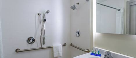 Une salle de bain équipée d’une douche, de barres d’appui, d’un porte-serviettes, d’un lavabo avec des articles de toilette et d’un miroir.