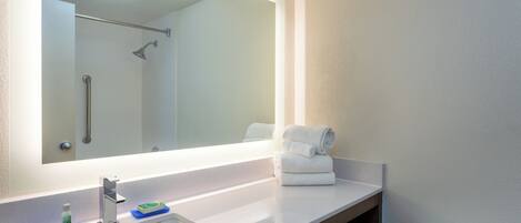A bathroom with a large mirror, a sink, a shower, and a toilet.